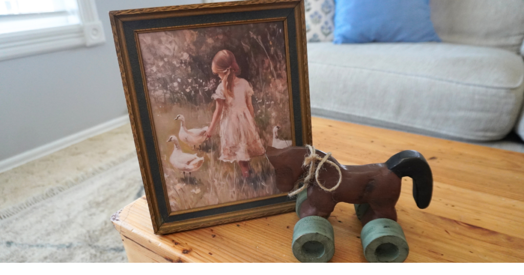 Art with image of girl and geese and wooden rolling horse.