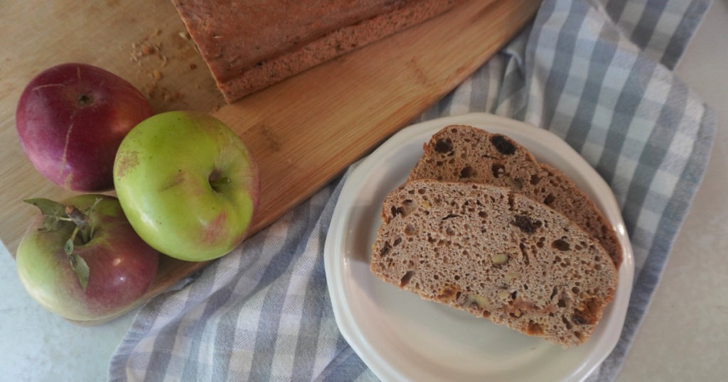 2 slices of bread on plate with apples on side with partial loaf of bread.