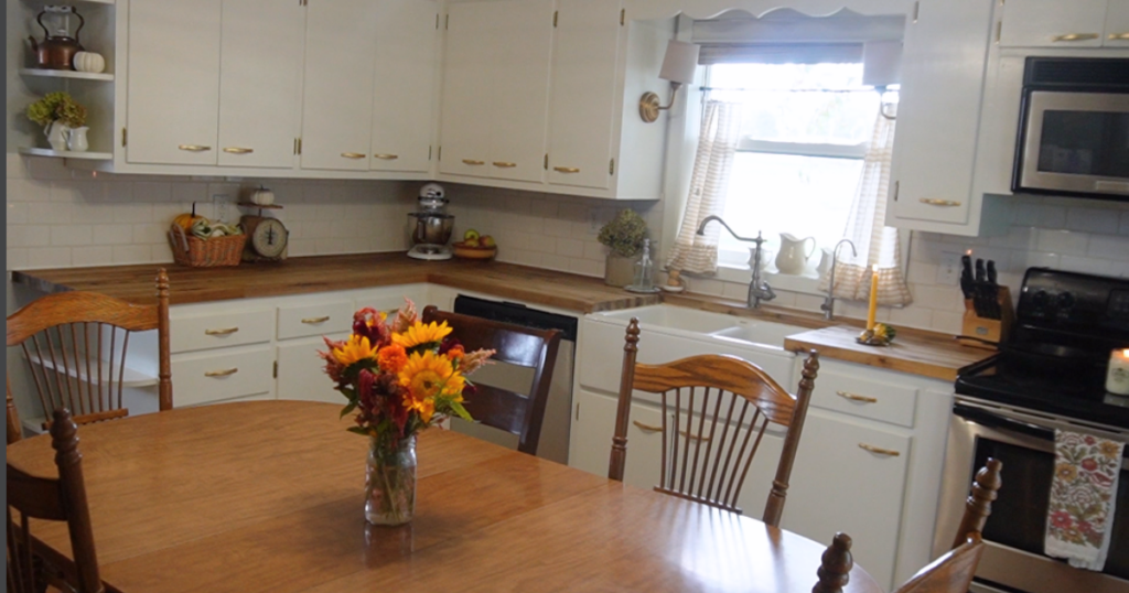 Eat in table in ktichen with flowers on table, candles on counter and dried hydrangeas in containers on counter and shelf