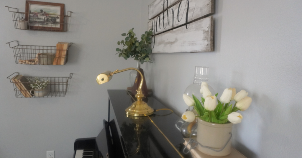 Tulips in crock on top of black piano with three wire shelves holding vintage crocks and books.