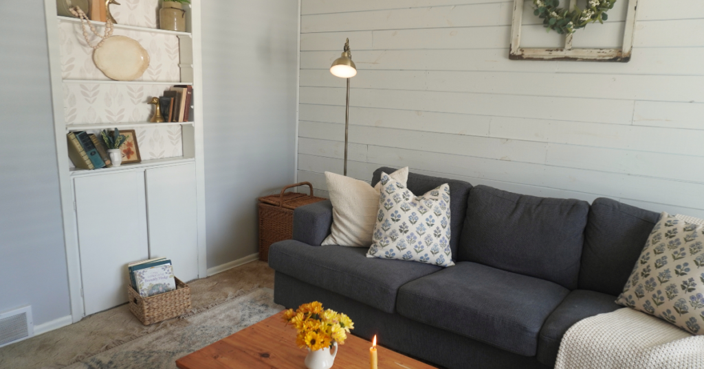 Living room with couch and pillows and built ins with tulips and books. Wood table with yellow flowers and candle.