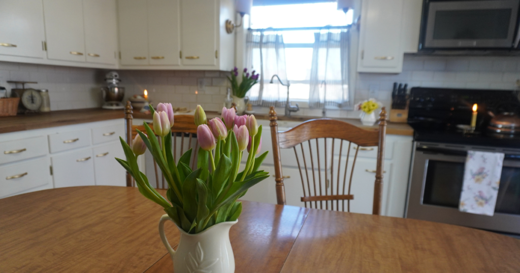 Close up of pink tulips on table with white kitchen cabinets in background.
