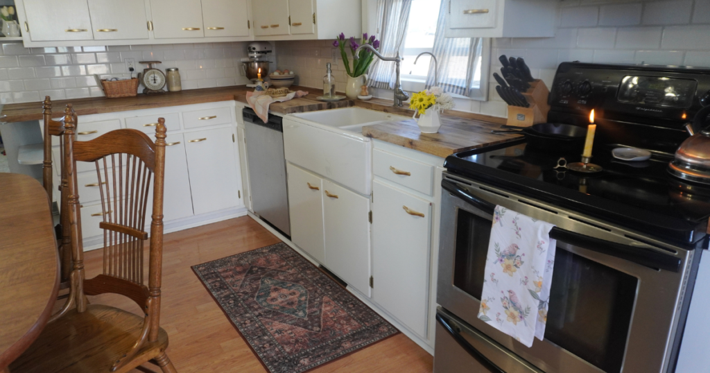 Stove with pink and yellow bird twel, flowers on the counter and kitchen cabinets in view.