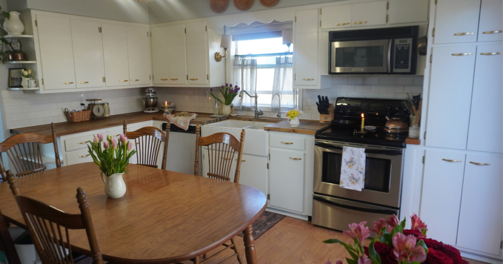 Spring kitchen with tulips in pitchers, white cabinets, and wooden kitchen table in center.
