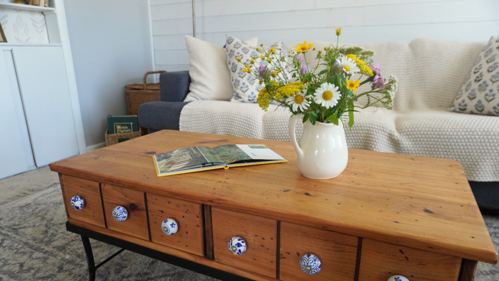 Wood coffee table with flowers in pitcher and couch in background