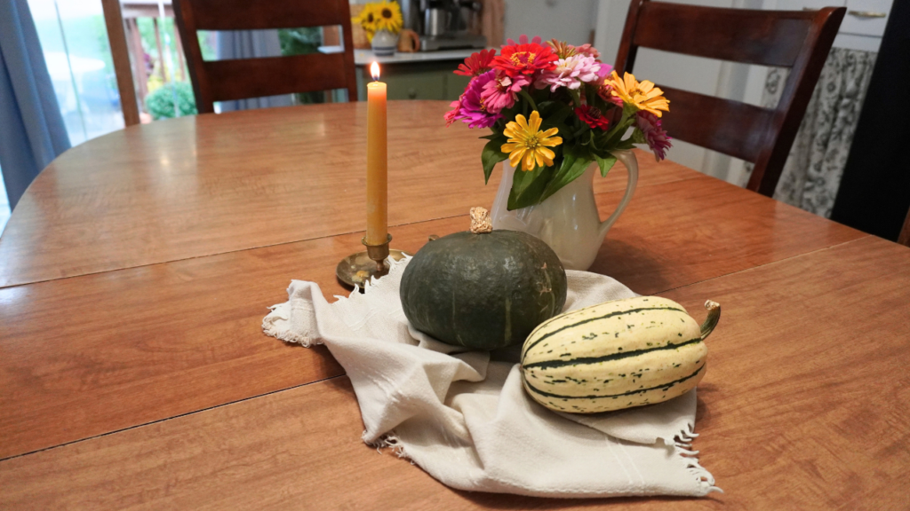 Flowers, pumpkins, candle on cream clothe on table.