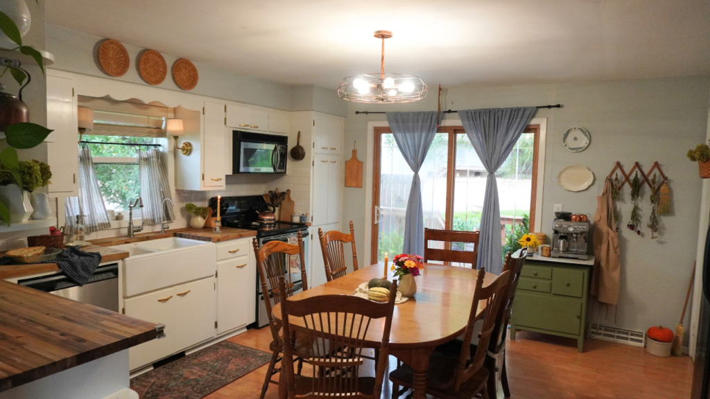 Kitchen view of table with pumpkins and flowers, counter with pie and apples and candle.