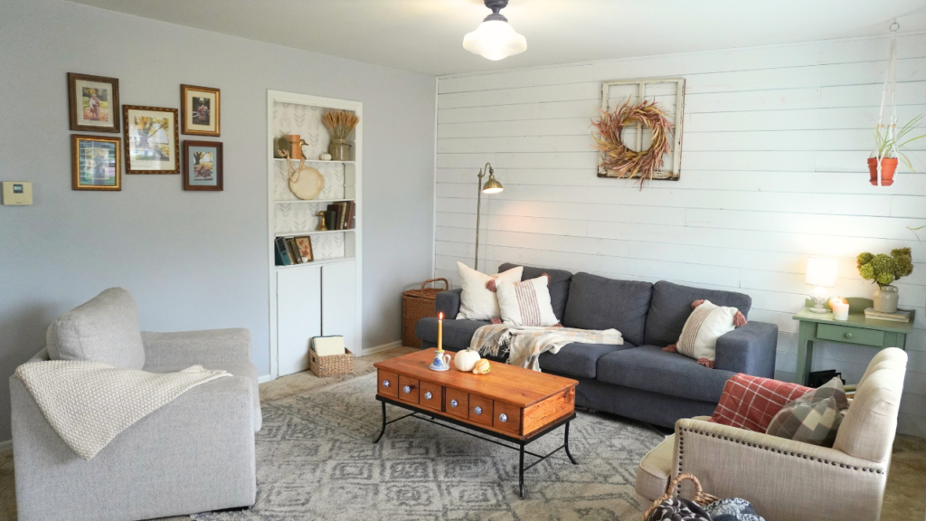 Living room with fall touches. Pumpkins on coffee table, wheat wreath and wheat stems hydrangeas on side table and candles lit.