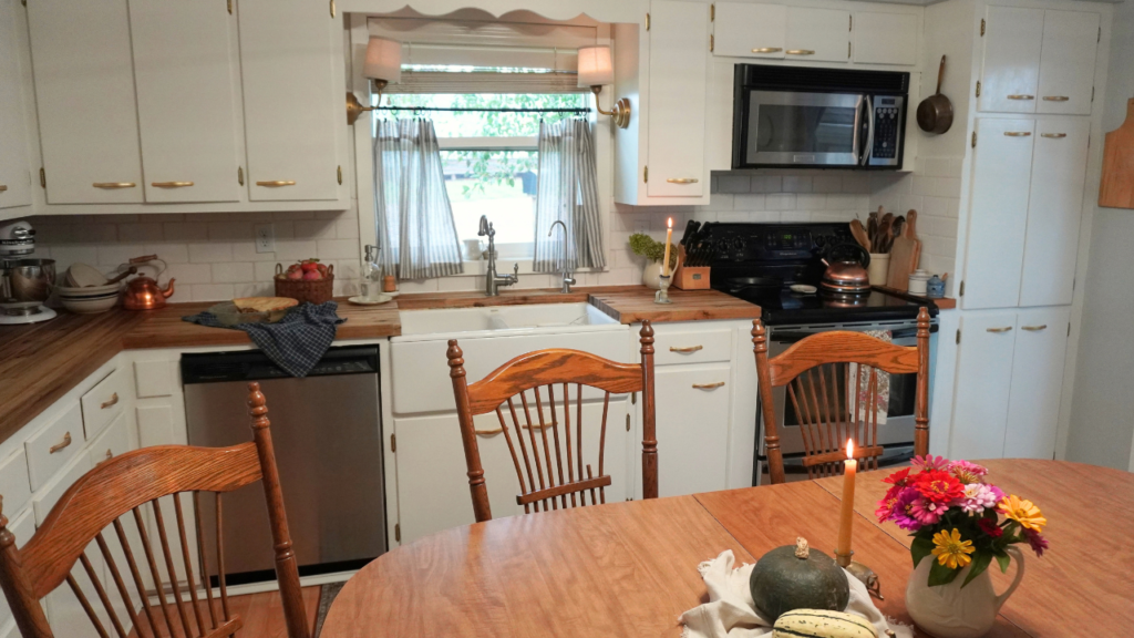 Half of table with pumpkins, candle and flowers on it. Counter and cabinets in back.